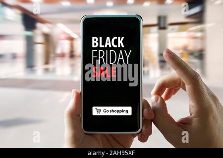 Hände halten Handy mit schwarzer Freitag Verkauf auf dem Bildschirm auf verschwommenes Bild der Shopping Mall. Kauf von Waren über das Internet in die mobile Anw Stockfoto