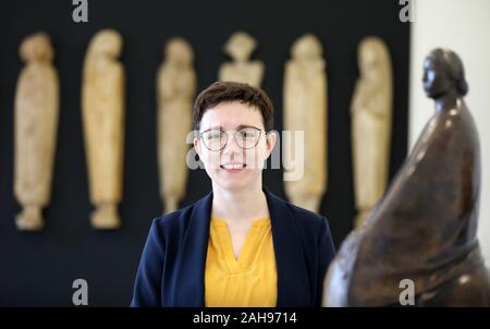 19 Dezember 2019, Mecklenburg-Vorpommern, Güstrow: Magdalena Schulz-Ohm, Geschäftsführer, steht in der Ernst-Barlach-Stiftung im Studio Haus vor der "Fries der Zuhörer' (1935) von Ernst Barlach (1870-1938), auf der rechten Seite die Skulptur 'Trauer (Sitzende Frau)" (Trauer (Sitzende Frau)) von 1913. Aus Anlass des 150. Geburtstags des Künstlers, die ständige Ausstellung im Studio Haus wird neu gestaltet. Foto: Bernd Wüstneck/dpa-Zentralbild/dpa Stockfoto