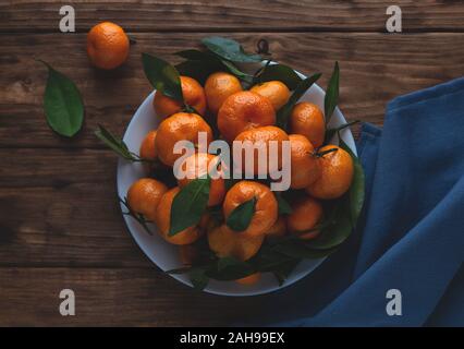 Mandarinen mit Blättern in einer Platte auf einem hölzernen Hintergrund. Horizontale Foto. Stockfoto