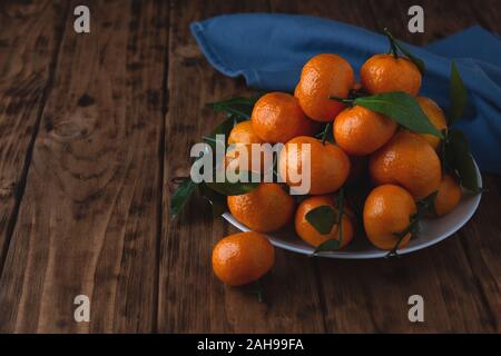 Cherry Tangerinen mit Blättern in einer Platte auf einem Holztisch. Stockfoto