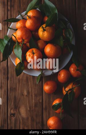 Mandarinen mit Blättern in einer Platte auf einem Holztisch. Ansicht von oben, Platz für Text. Stockfoto