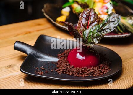 Vanille - Kokos-mousse mit Schokolade und Rote-Bete-Sauce. Dessert in Form von Rüben ist auf eine ungewöhnliche Platte in Form einer Schaufel, serviert. Stockfoto