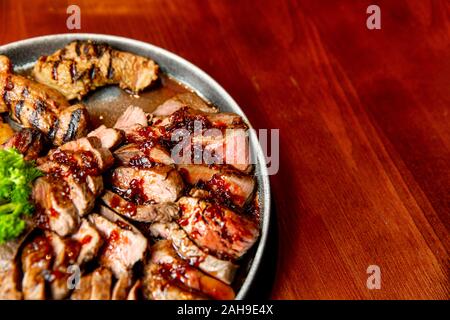 Frische, saftige Sortiment von geschnittenen Fleisch vom Grill, die auf eine große und runde Platte liegt, mit Petersilie auf der Oberseite dekoriert. Stockfoto