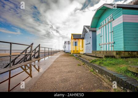 Reihe der traditionellen hölzernen Umkleidekabinen am Strand an der Promenade neben einem Sand- und Kiesstrand entfernt an der Küste von Norfolk Stockfoto