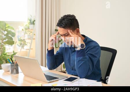 Das Gefühl erschöpft. Frustrierte junge Bart Mann massieren den Kopf und die Augen, während er an seinem Arbeitsplatz im Büro geschlossen Stockfoto
