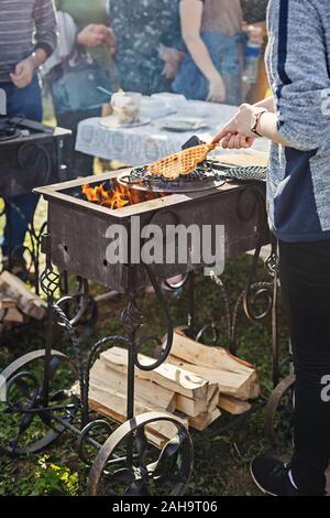 Waffeln backen am offenen Feuer im Freien in einem Gehämmert gusseisernen Grill. Defokussiertem Hintergrund von Menschen für Waffeln warten. Stockfoto
