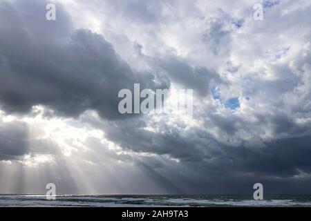 Sonnenstrahlen durch die Wolken von einer dramatischen stürmischen Himmel über dem Mittelmeer mit schäumenden Wellen brechen. Israel Stockfoto