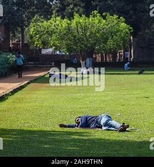 Bhubaneshwar, Orissa, Indien - Februar 2018: Ein Mann schläft im Sonnenlicht auf dem grünen Gras eines öffentlichen Gartens. Stockfoto