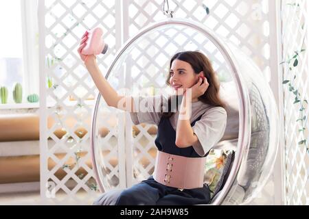 Das Mädchen sitzt in einem transparenten Stuhl und nimmt eine selfie ein Foto auf dem Instant Kamera Stockfoto