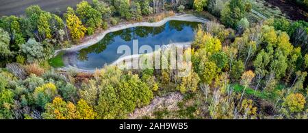 Luftbild aus einer Höhe von 100 Meter auf einer künstlichen blau-grünen Teich mit Bäumen surroundingin, der die Wolken reflektiert werden. Stockfoto