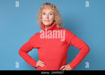 Casual kaukasischen reife Frau in Rot Pullover stehend an der Kamera, und achten Sie darauf in ihrer Stärke auf der Suche überzeugt. Studio gedreht. Positive facial menschlichen emoti Stockfoto