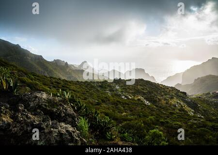 Spanien, Teneriffa, dunkle Wolken regen Sturm an stürmischen Tag mit Sonne über den Bergen von Masca Schlucht am Meer Küste, Blick über grüne Natur Landschaft Stockfoto