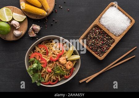 Blick von oben auf die lecker spicy thai Nudeln mit Krabben in der Nähe von Stäbchen, Gewürze, Kalk und Mais auf Holz- graue Oberfläche Stockfoto