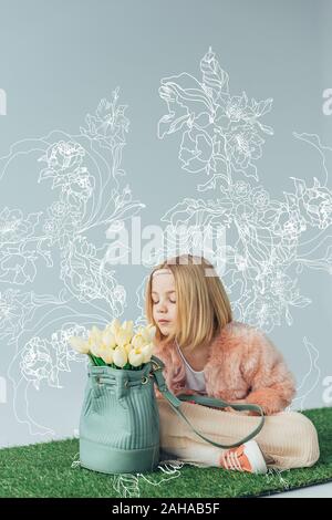 Cute kid mit gekreuzten Beinen duftende weiße Tulpen im Beutel auf grau mit weißen Blüten Illustration isoliert Stockfoto