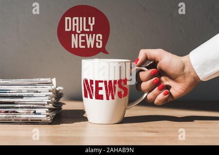 7/8-Ansicht von Frau mit weißer Schale mit Nachrichten Beschriftung auf dem Holztisch in der Nähe von Pile verschiedener Zeitungen und Sprechblase Abbildung mit Zähler Stockfoto