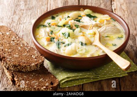 Herzhafte Cremesuppe mit Gnocchi, Huhn und Spinat mit Brot in der Nähe serviert in einer Schüssel auf dem Tisch. Horizontale Stockfoto