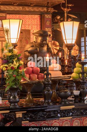 Tokyo, Japan - 7. Januar 2020: mochi's neue Jahr Reis, Clementine und Äpfel Angebote vor eine hölzerne Statue der Daikokuten japanische Gottheit. Stockfoto