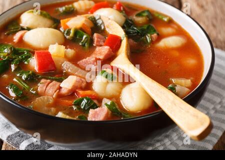 Würzige Tomatensuppe mit Gnocchi, Würstchen, Spinat und Gemüse close-up in einer Schüssel auf dem Tisch. Vertikale Stockfoto
