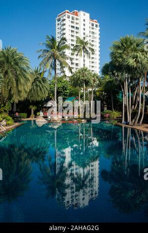 16.11.2019, Phuket, Thailand - Palmen am Pool des Mövenpick Resort & Spa Karon Beach Phuket. Der Wolkenkratzer im Hintergrund ist Stockfoto