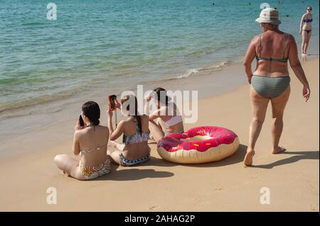 17.11.2019, Phuket, Thailand - Urlauber sitzen auf dem Sand am Strand von Karon und Blick auf das Meer. Der Strand ist ein beliebtes Ziel für C Stockfoto