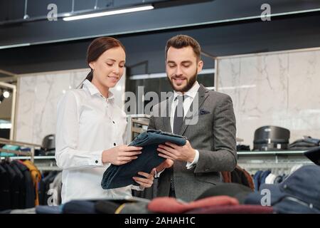 Junger Mann in Anzug Wahl ihm neue Jeans und freundliche Verkäuferin helfen Stockfoto