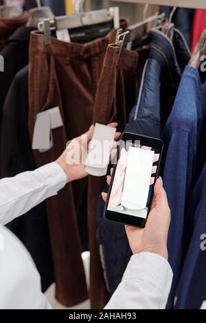 Die Hände der weiblichen Shop Assistant mit Smartphone, Foto, Preis am Tag Stockfoto