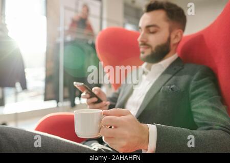 Hand des Jungen gut gekleidete Geschäftsmann bei einer Tasse Kaffee entspannen im roten Sessel Stockfoto