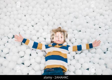 Cute little boy in casualwear outstretching seine Arme unter weißen Luftballons Stockfoto