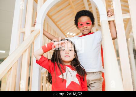 Asiatische Mädchen nahe stehend zu den kleinen afrikanischen Jungen beim Spielen im Kindergarten Stockfoto