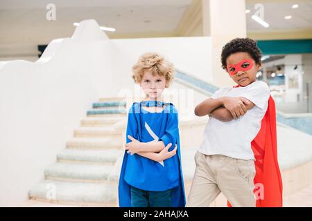 Zwei kleine interkulturelle Jungs in Kostümen von Superman auf Sie auf der Suche Stockfoto