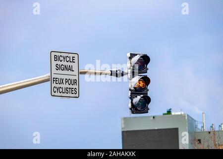 Eine Ampel für einen Radweg Gelb, Warnung Radfahrer zum Stillstand kommen. Die pendelaufhängung Signal hat ein Zweisprachiges Schild in englischer und französischer Sprache, ein Stockfoto