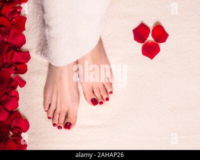 Schöne weibliche Füße auf frotteehandtuch mit Rosenblättern. Jar und das Rohr der Pflegecreme. Wellness und Hautpflege. Stockfoto