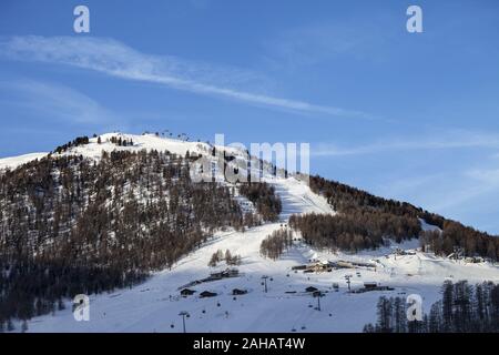 Verschneite Skipiste mit Liften, Spuren und Wald im Winter Berge am sonnigen Morgen. Italienische Alpen. Livigno, Region Lombardei, Italien, Europa. Stockfoto