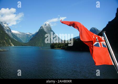 Der rote Stern, ein Roter maritime Version der NZ Flagge, flattert auf einem Sightseeing Fähre auf dem ruhigen, tiefblauen Milford Sound im Fjordland Region Neuseelands Stockfoto