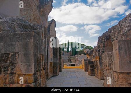 Alten verfallenen Mauern, gelbes Quadrat der Amphitheater, grünen Bäumen und blauer Himmel mit weißen Wolken. Römische Stadt Italica in Sevilla, Spanien Stockfoto