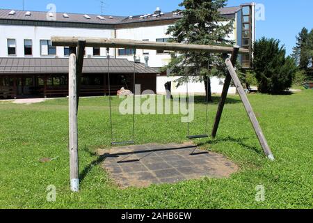 Verfallenen alten hölzernen Retro Vintage outdoor öffentlichen Spielplatz ausrüstung in Form von Swing mit zwei Sitzen in verlassenen Bürogebäude Hinterhof Stockfoto