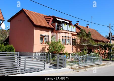 Kleine suburban Family House mit neuen dunkel rosa Fassade und Balkon mit Blumen mit Garten pflanzen und Metall Zaun umgeben gefüllt Renoviert nächste Stockfoto