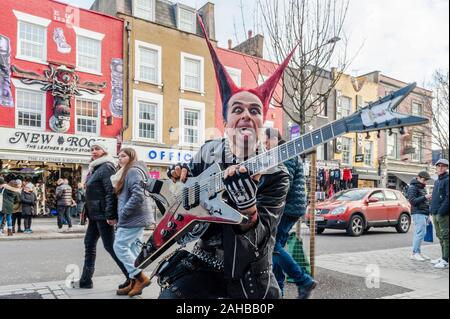 Mann in Punk-Rocker-Kleidung mit Stachelhaar und einer Gitarrenpose für Touristenbilder an der Camden High Street, Camden, London, Großbritannien. Stockfoto