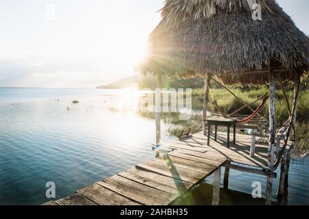 Dock bei Sonnenuntergang mit Sonnenstrahlen Hintergrundbeleuchtung am See Itza, El Remate, Peten, Guatemala Stockfoto