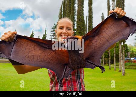 Lustige Porträt eines jungen Mädchens in den Händen halten, riesige Flying Fox (Obst bat). Tag Tour auf Familie Sommerurlaub mit Kindern. Beliebtes Reiseziel Stockfoto