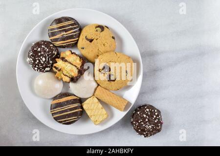 Leckere frisch gebackene Plätzchen sitzen fröhlich auf einem einfachen weißen Teller auf einem marmorboden Hintergrund. Zimmer für Kopieren. Stockfoto
