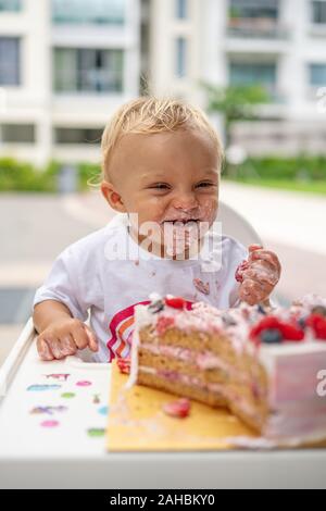 Ein Baby essen lecker Geburtstagskuchen mit seinen Händen mit Kuchen um seinen Mund Stockfoto