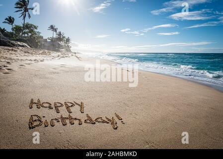 Happy Birthday in den Sand auf dem Sunset Beach in Hawaii geschrieben mit Palmen und das Meer im Hintergrund Stockfoto