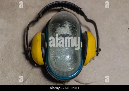 Gelbe industrielle Kopfhörer im industriellen Wandleuchte mit einem Glaskolben. Staubige Wand in der Werkstatt. Schießen von unten nach oben. Stockfoto