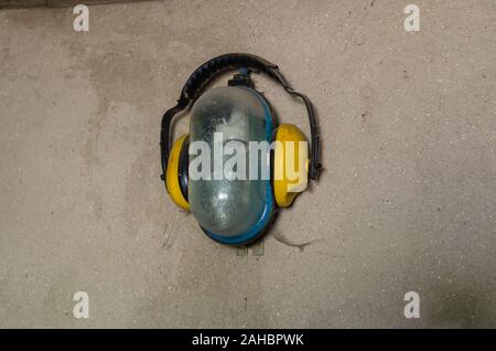 Gelbe industrielle Kopfhörer im industriellen Wandleuchte mit einem Glaskolben. Staubige Wand in der Werkstatt. Schießen von unten nach oben. Stockfoto