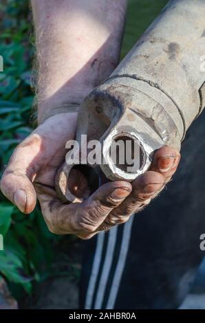 Ein Mann hält einen alten rostigen Auto Kreuzgelenk. Den Einbauort der Steg mit Lager ist poliert. Entwicklungsbiologie konzentrieren. Vertikal Stockfoto