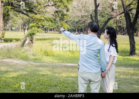 Asiatische Paare werden aufgezeigt und Aufmerksamkeit auf etwas im Garten zahlen. Asiatische Paare halten sich an den Händen und im Park. Nach männlichen und weiblichen Cou Stockfoto