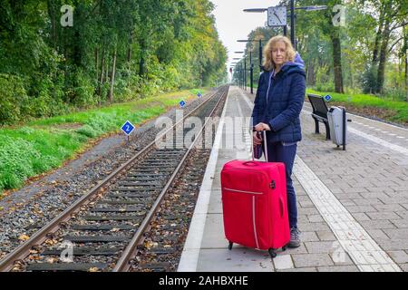 Kaukasische Frau mit roten Koffer stehen am Bahnhof Stockfoto