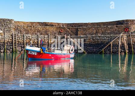 Rotes Fischerboot vor dem Hafen von Clovelly, diesem berühmten Fischerdorf mit Blick auf die Hafenmauer und Holzleitern, Südwesten Stockfoto