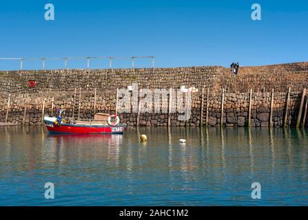 Ein rotes Fischerboot, das neben der Hafenmauer im ikonischen Fischerdorf Clovelly, einem malerischen, charmanten Dorf in diesem Urlaubsziel, festgemacht ist. Stockfoto